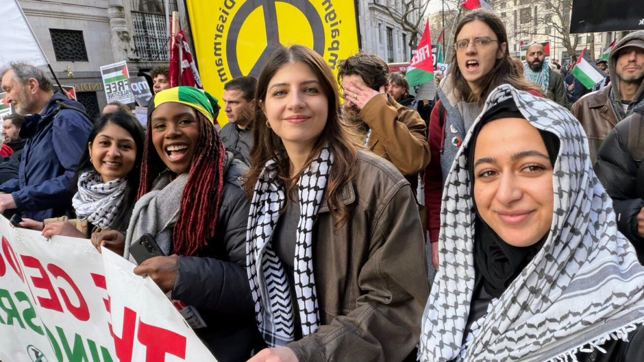 A group of women wearing keffiyehs hold a banner on a march