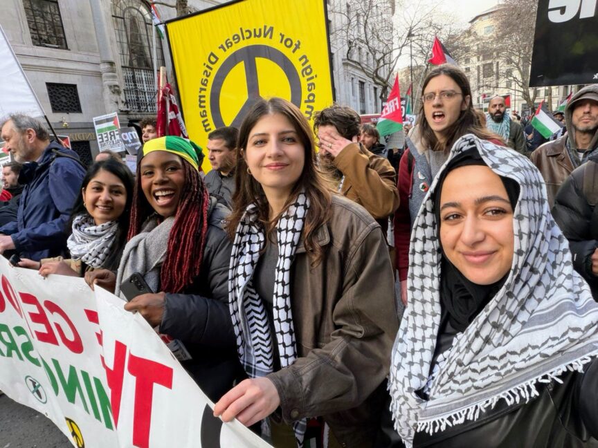 A group of women wearing keffiyehs hold a banner on a march