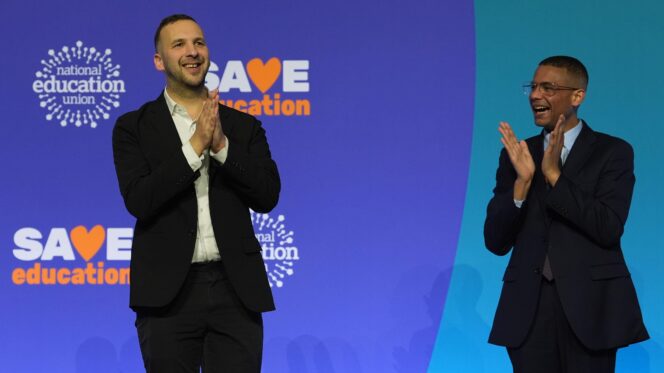 Two men stand beside one another clapping