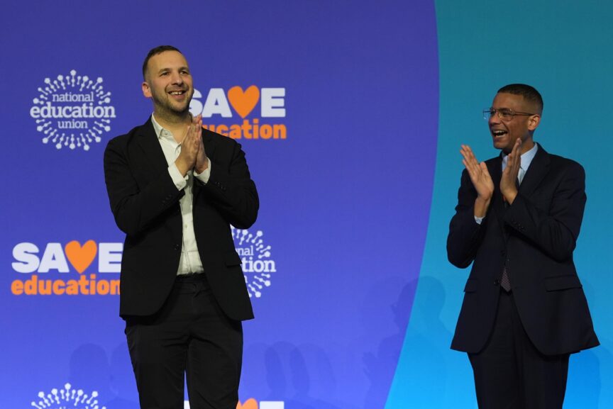 Two men stand beside one another clapping