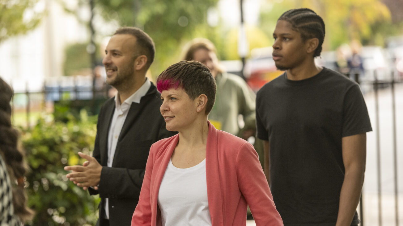 A woman in a pink jacket walks flanked by two men