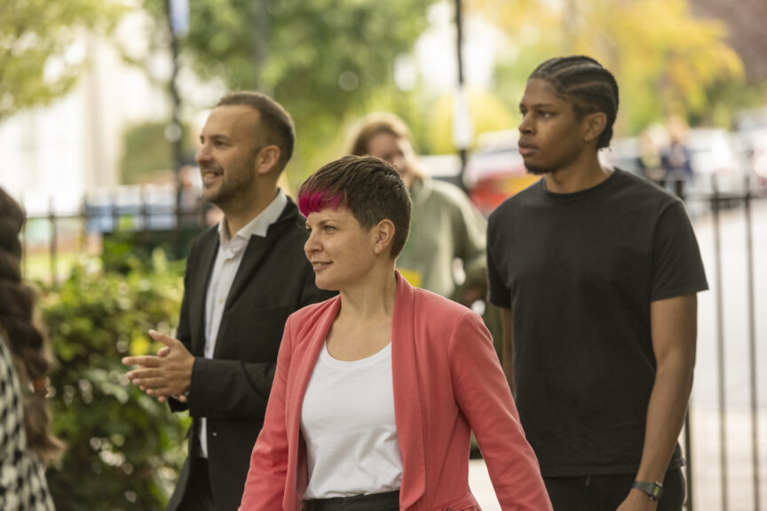 A woman in a pink jacket walks flanked by two men