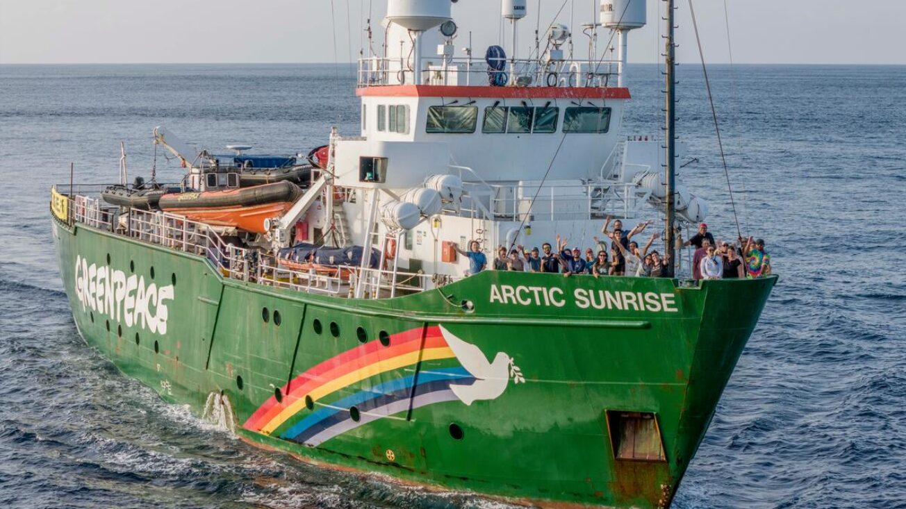 A large boat called Arctic Sunrise sails with lots of triumphant people on board