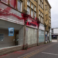A Barclays bank with a cracked window, sprayed with red paint.
