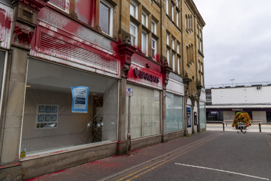 A Barclays bank with a cracked window, sprayed with red paint.