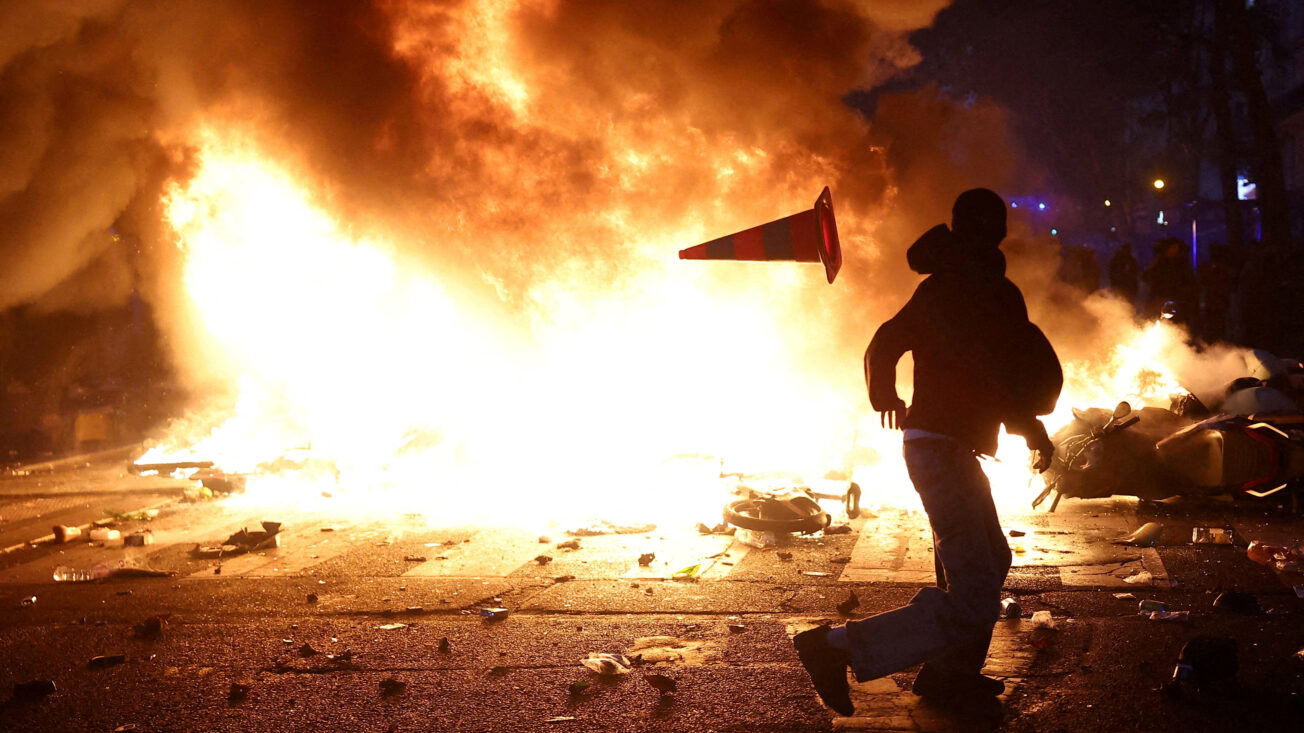 A man throws a plastic traffic cone through a burning barricade in Paris as part of nationwide protests called by the 'Yellow Vests' movement, joined by French high school and university students, teachers, trade unions and parents demanding better school conditions. Photo: REUTERS/Abdul Saboor